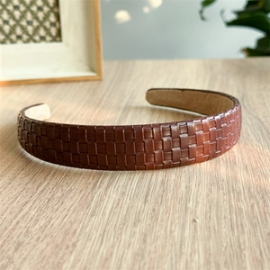 Detail of wide brown leather headband with woven texture on a natural wooden table