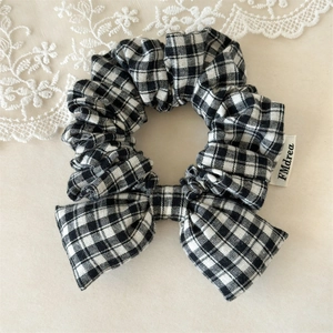 Detailed view of black and white plaid scrunchie with bow and woven label design