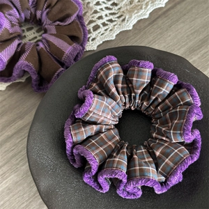 Detailed texture of plaid fabric scrunchies with purple velvet trim on a wooden table