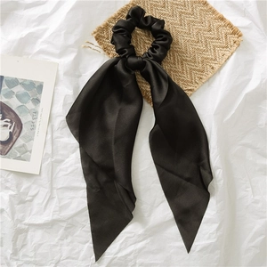 Close-up of a black satin hair scrunchie with long ribbons on a textured background