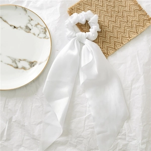 Close-up of elegant white satin ponytail streamer scrunchie on marble tray and textures