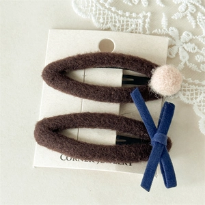 Gros plan de barrettes à cheveux en peluche marron avec nœud bleu et pompon rose sur dentelle