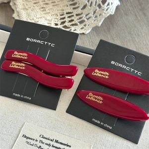 Set of four dark red acetate hair clips with gold metal grips on a display card