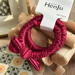 Close-up of elegant burgundy satin ruched scrunchie with bow detail on card