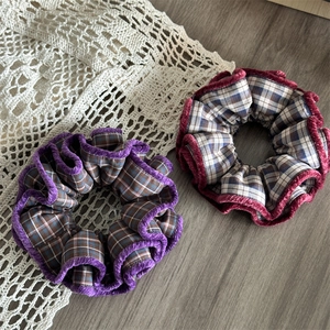 Flat lay detail of purple and burgundy plaid fabric scrunchies with soft velvet piping