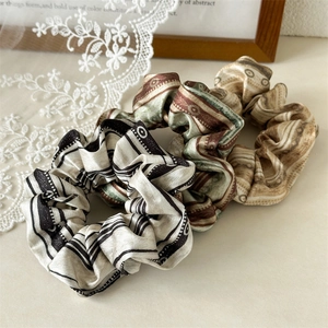 Three vintage satin scrunchies with geometric and striped patterns on a lace background