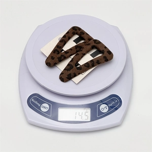 Macro shot of a pair of plush leopard print BB hair clips on a scale showing 14.5g weight