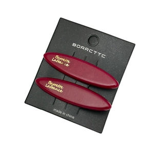 Pair of deep red acetate oval hair clips with gold lettering on black display card