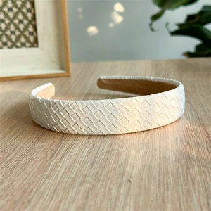 Detailed view of white woven leather headband featuring elegant crisscross pattern on wood
