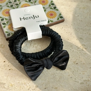 Detail of elegant black satin bow hair scrunchies on white display card with sunlight