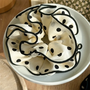 Detailed macro view of large cream scrunchie with black polka dots and stitched edges