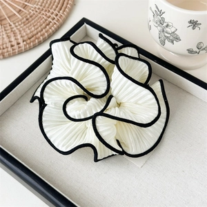 Detailed view of large pleated beige hair scrunchie with black contrast piping on edge