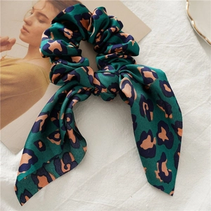 Detail of silk emerald leopard print scrunchie with bow ribbon on white texture