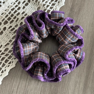 Detailed shot of plaid fabric scrunchie with purple velvet trim and pleated texture