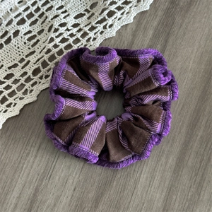 Detail of purple plaid fabric scrunchie with fuzzy trim on grey wood background