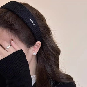 Detail of black textured wide headband with True Fitted label worn by model with jewelry