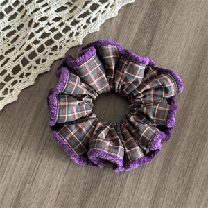 Detail of a large plaid hair scrunchie with purple chenille edge on a wooden surface