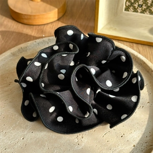 Close-up of black and white polka dot silk scrunchie with detailed ruffled texture on beige plate
