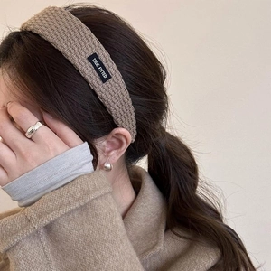 Close-up of beige knitted headband with True Fitted label worn by model in wool coat