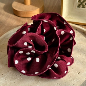 Detail of burgundy polka dot scrunchie with soft ruffled fabric texture on beige plate