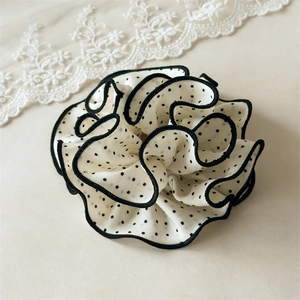 Detailed view of polka dot chiffon scrunchie with black trim on creamy background