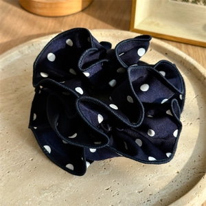 Detailed view of large dark blue polka dot silk scrunchie on a stone display plate