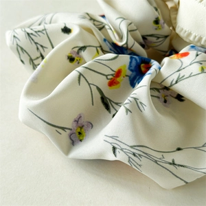 Close-up of the delicate floral pattern and soft fabric texture of the cream scrunchie