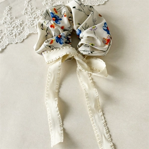 Close-up of floral scrunchie with long ribbon bow and ruffled edges in soft silk