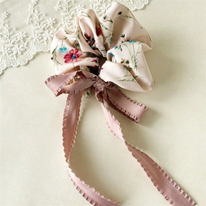 Detail of pink floral scrunchie with long chiffon ribbons on a cream lace background