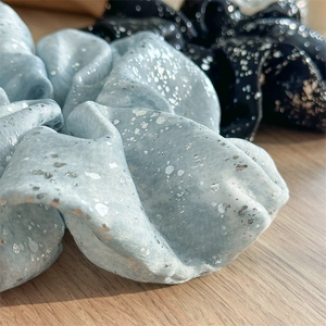 Detailed close-up of light blue and black scrunchies with silver foil patterns on satin fabric