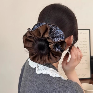 Close-up of a brown satin and blue floral scrunchie worn on a high ponytail in a home setting