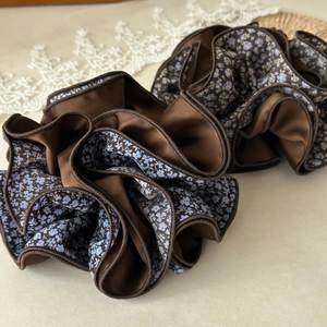 Close-up of brown satin scrunchie with hidden blue floral print and pleated detail