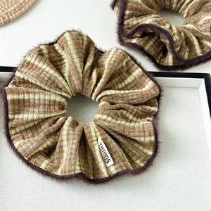 Detail of striped fabric scrunchie with brown faux fur trim and white woven label tag