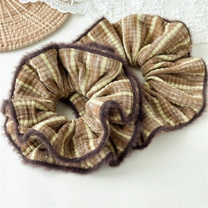 Close-up of brown striped scrunchies with plush trim on a minimalist textured background
