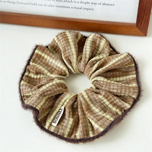 Close-up of striped scrunchie with plush trim and white label on a cozy background
