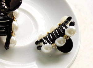 Detail of elegant black resin hair claw clip with white pearls and sparkling rhinestones