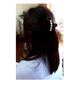 Detail of elegant black hair claw clip with five white pearls worn on back of head