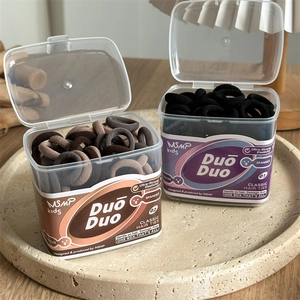 Detail of high-elasticity hair ties in a transparent box on a stone display tray