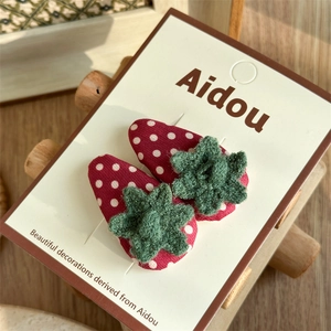 Détail de deux barrettes fraises rouges avec feuilles tricotées vertes sur carte