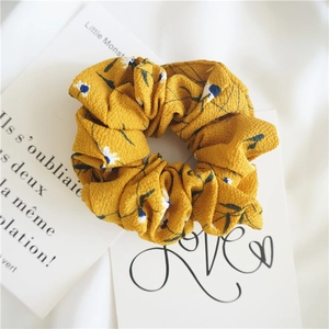 Close-up of yellow floral chiffon scrunchie with white daisies and textured pleats