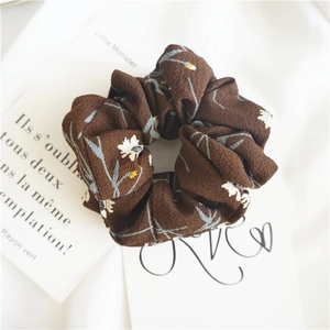 Detailed macro view of retro brown chiffon scrunchie with delicate white daisy floral pattern