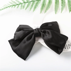 Macro shot of a large black satin triple-layered bow hair clip with a sleek silky texture