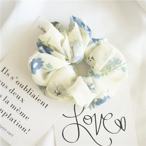 Close-up of a floral chiffon scrunchie with blue and grey flower patterns on cream fabric
