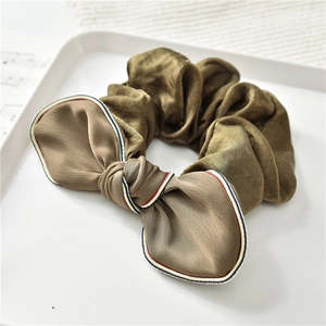 Dettaglio scrunchie in seta marrone oliva con fiocco a righe su un piatto bianco