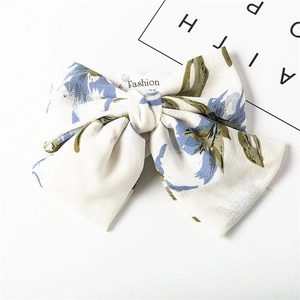 Detail view of large white chiffon bow hair clip with blue and green floral patterns