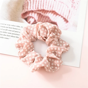 Détail d'un chouchou en mousseline à pois roses sur un fond de magazine décoratif