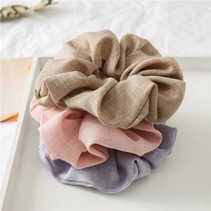 Close-up of linen-textured hair scrunchies in brown, light pink, and lavender hues