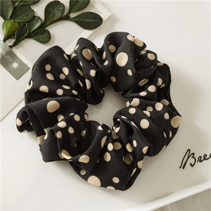 Close-up of black scrunchie with beige polka dots on a minimalist white tray