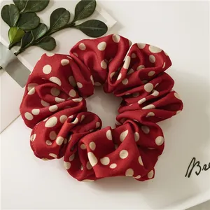 Close-up of burgundy polka dot scrunchie on a white tray with green leaf accents