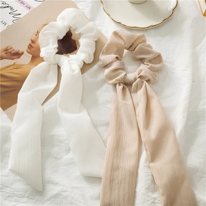 Detail of white and beige ribbon scrunchies with elegant pleated texture on a fabric surface